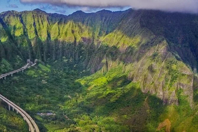 Steep green ridges of the Koolau mountains above a highway curving along a valley