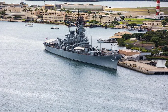 Das graue Schlachtschiff Missouri an einem Pier in Pearl Harbor, dahinter niedrige Gebäude