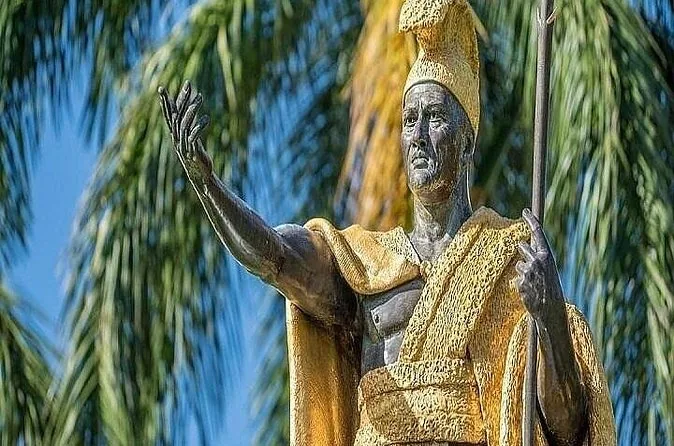 Die bronzene King-Kamehameha-Statue mit goldenem Umhang, die einen Arm vor Palmwedeln hebt